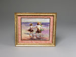 Framed artwork of two children on a beach with a gold frame.