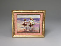 Framed artwork of two children on a beach with a gold frame.