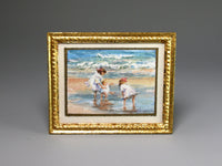 Framed miniature artwork of children playing on a beach with a gold frame.